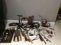 Assorted antique and other hand tools laid out on floor, including hammers, screwdrivers, files, measuring tape, hand drill, copper coil, wrenches, saw blade and various other hand tools.