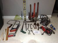 Full overview of assorted tools laid on floor including pipe wrenches, hacksaws, levels, wrenches, and power tools.