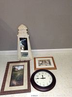 Photo of all four items including lighthouse mirror, two framed prints, and clock arranged on floor against wall.