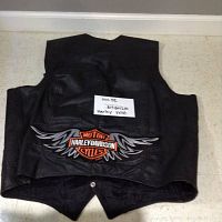 Back of a black leather vest showing large Harley Davidson Motor Cycles logo with wings embroidered in orange and silver thread.