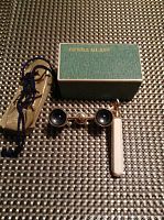 Photo showing the vintage opera glasses next to the original box and beige drawstring pouch on woven textured surface.