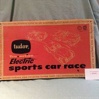 Top view photo of the 1959 Tudor Electric Sports Car Race original toy box showing red-orange graphic with black text and illustrations of sports cars in racing motion.