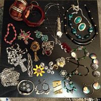 Full assortment of costume jewelry including bracelets, necklaces, brooches, earrings, and watches displayed on a black surface.