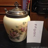 Front view of antique biscuit jar with floral decoration and silver-plated handle and lid, showing overall appearance and artwork on the ceramic body.