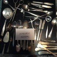 Top view showing the full assortment of flatware spread out, highlighting the variety in types and sizes of pieces with a note indicating lot number/description.