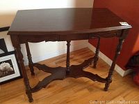 Front angled view of dark stained decorative occasional table with turned legs and stretcher base, showing aged wear.