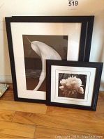 Two framed black and white floral prints leaning against wall on wooden floor, one print larger than the other, featuring flowers in monochrome.