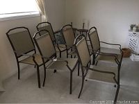 Six brown metal frame patio chairs with beige mesh fabric seats and backs arranged indoors near a window on concrete floor.