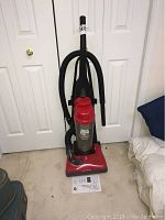 Front view of red Dirt Devil Featherlite vacuum cleaner with attached hose, user manual on floor.