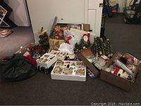 Wide view of Christmas lot showing multiple boxes and bags containing village buildings, linens, decorations, and other holiday items.