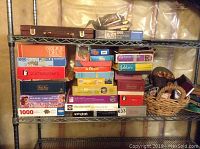 Shelf showing stacked boxes of board games, puzzles and card games including Bridge a Deux puzzle, Scattergories, Bingo, Yahtzee, and Trivial Pursuit