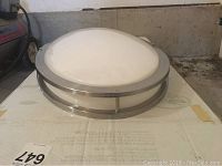 Top view of the circular ceiling light fixture on its original box, showing the frosted dome diffuser held by the metal frame.