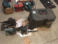 Various tools including electric palm sanders, gray plastic step stool toolbox, sandpaper sheets.
