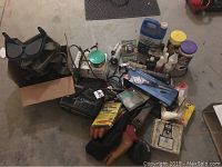 Overview photo showing numerous automotive and household maintenance items on concrete floor including chargers, cleaning products, gloves, and tools packed together.