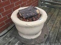 Full view of the round beige fire pit with artificial logs and lava rocks inside, showing size and overall appearance.