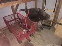 Red metal mesh trolley with air tires, black hand pump inside trolley bed, rusted metal wheelbarrow behind it, black and yellow dolly to the side.