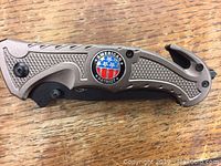 Closed folding knife showing metal handle with textured grip and American Patriot emblem.