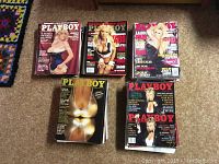 Five Playboy magazines arranged in two rows on a crocheted blanket background. Visible covers show crop top and bathing suit models. One magazine cover from 1984 featuring Suzanne Somers is visible.