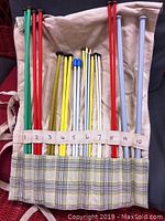 Photo showing knitting needles in various colors (red, green, yellow, white, gray) organized and labeled from sizes 2 to 10 in a beige plaid folding fabric case.