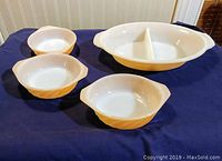 Front view of the entire vintage Fire King luster ovenware set featuring one divided baking dish and three side dishes with a lustrous amber/golden exterior and white interior.