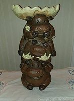 Front view of the carved moose bird feeder showing three moose stacked with leaf-shaped bowl at top