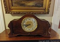Front view of walnut case mantle clock with circular clock face featuring Arabic numerals and ornate center.