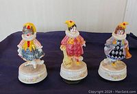 Three clown music boxes displayed in a row on a dark cloth background.