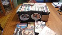 Box filled with approximately 50 DVDs of assorted titles. Two cases opened to show disc label for The Untouchables. Surface and case condition are visibly lightly used.