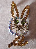 Front view of vintage open work rabbit brooch with amber, aurora borealis, and peridot rhinestones detailing ears, face frame, and eyes.