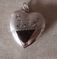 Front side of heart-shaped sterling silver locket showing engraved swirl and star design