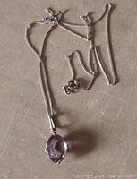 Front view of the amethyst pendant on sterling silver chain placed on a neutral surface showing detail of gemstone and chain texture.