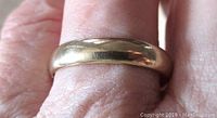 Close-up photo showing the rounded, polished surface of the yellow gold band worn on a finger.