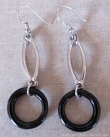 Pair of sterling silver drop earrings with black onyx circular pendants on a fabric background.