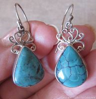 Close-up of one turquoise drop earring showing teardrop shape and silver scroll design