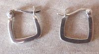 Pair of silver square hoop earrings displayed flat to show shape and condition