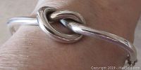 Close-up side view of the sterling silver knot motif on the bangle bracelet showing smooth polished surface and shape detail