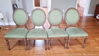 Four solid wood dining chairs with green upholstered seats and backs arranged in a row on hardwood floor.
