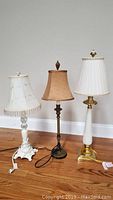 Three small lamps standing side by side on hardwood floor with visible cords, displaying overall design and size