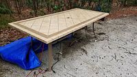 Full view of large outdoor rectangular table with beige tiled top and metal legs on a gravel surface.
