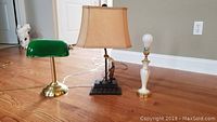 Three assorted lamps on a wood floor: green glass bankers lamp, golfer ceramic lamp with beige shade, and small white ceramic lamp with exposed bulb.