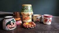 Autumn-themed ceramic and decorative candle holders arranged on a dark wooden surface against a dark blue background wall, featuring pumpkin and leaf motifs.