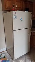 Image showing a white GE refrigerator with top freezer, minor wear and magnets on door, placed between kitchen cabinets.