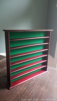 Photo of a wooden golf ball display case with six horizontal shelves and green felt backing, angled to show depth and design.