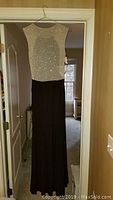 Full view of the evening dress hanging on a hanger showing the sparkling silver bodice and long black skirt.