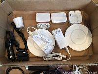 Box containing two white Belkin wireless charging pads, Apple wired earbuds in white case, car charging adapters, and power adapter cords.