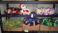 Wreaths arranged on shelving including floral, patriotic, and pet plush dog.