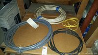 Four coils of electrical cord in black, gray, white, and yellow on cardboard surface.
