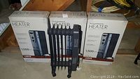 Three black oil-filled radiator heaters, each with multiple fins, caster wheels, and control panels, displayed in front of their original boxes showing product details.
