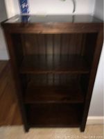 Front view of the wooden bookcase showing three shelves and visible scratches on the second shelf.