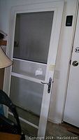 Full view of white screen storm door installed indoors. Shows screen section at top with glass panel and bolt lock with handle on right side.